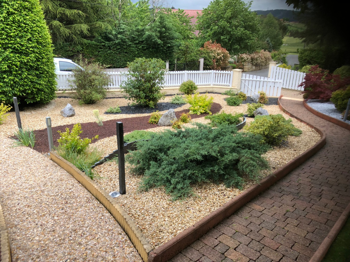 Jardin sec avec olivier, statue et gravier coloré Aménagement paysager méditerranéen avec statue blanche, gravier ocre et gris, olivier, et gazon synthétique près d'un mur beige.