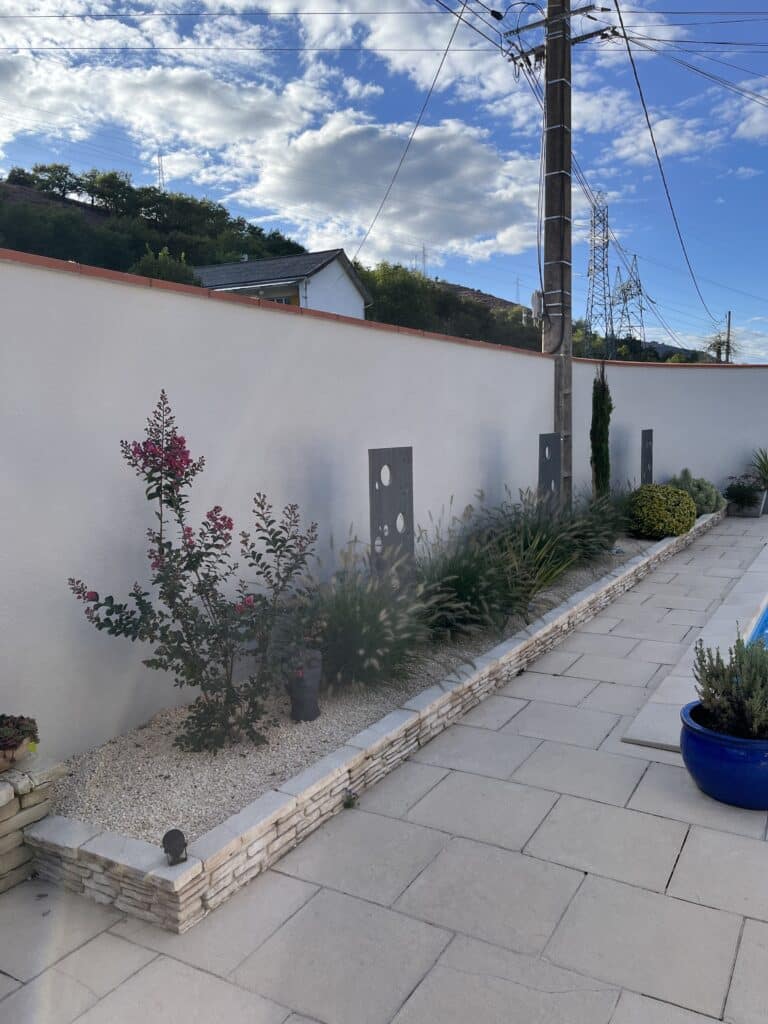 Aménagement Jardin Moderne : Parterre, Carrelage et Fleurs Allée carrelée à côté d'un parterre de gravier blanc, une plante à fleurs roses, des herbes ornementales et des décorations murales modernes.